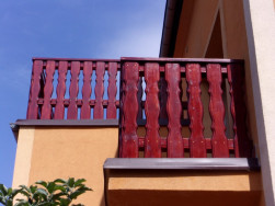 Balkonové zábradlí z ozdobných sloupků v červeném odstínu. Tohle, ale není krycí barva, toto je silnovrstvá lazura v odstínu Rosewood.
