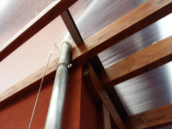 Okapové svody ze střechy domu prochází polykarbonátovou střechou.