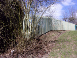 Dřevěný plaňkový plot ve svažitém terénu.