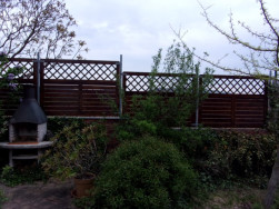 Pohled na hotový plot přichycený na zděnou zídku pomocí kovových sloupků.