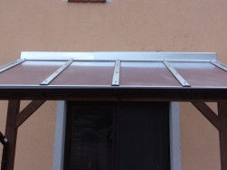 Utěsnění pultové střechy na zdi domu pomocí těsnící pásky překryté plechem.