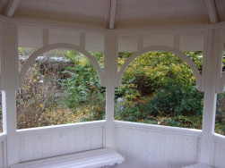 Pohled z vnitřku altánu na bílé ozdobné oblouky které drží altán pohromadě v horní části