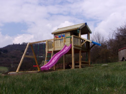 Dřevěný dětský domek s terasou na kterou vede žebřík s barevnými stupínky