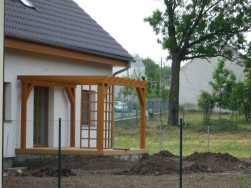 Barevné provedení pergoly ladí s rámy dveří i s dřevěným podbitím domu