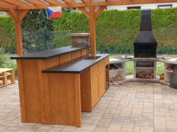 Venkovní kuchyně umístěná pod pergolou na vydlážděné terase u venkovního zahradního grilu