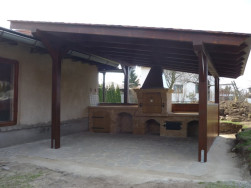 Pergola s pultovou střechou, která má dlouhý přesah nad střechou víkendové chalupy